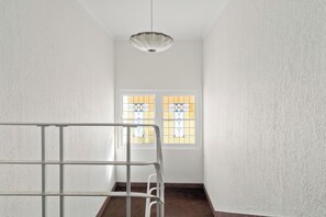 A narrow hallway with a metal railing, a ceiling light fixture, and two windows with stained glass. - Bondi Beach Apt with Rooftop Ocean Views (Bondi Beach)