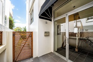 A modern building with a glass door entrance, a wooden gate, and a bicycle parked inside. - Bondi Beach Apt with Rooftop Ocean Views (Bondi Beach)