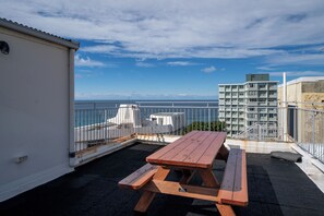 A rooftop terrace with a wooden picnic table, a white building, and a view of the sea. - Bondi Beach Apt with Rooftop Ocean Views (Bondi Beach)
