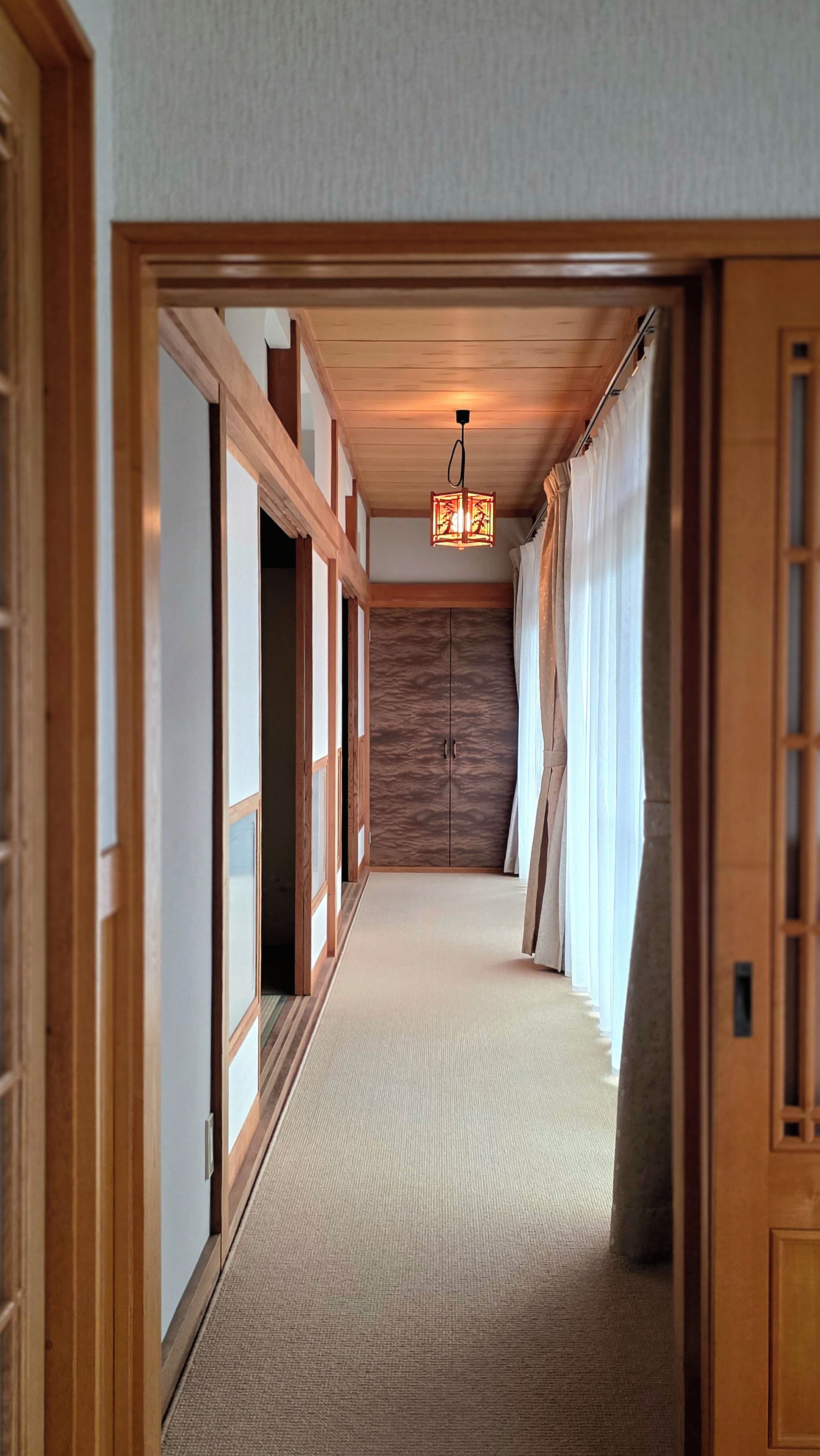 A hallway with a wooden door frame, a carpeted floor, and a hanging light fixture.