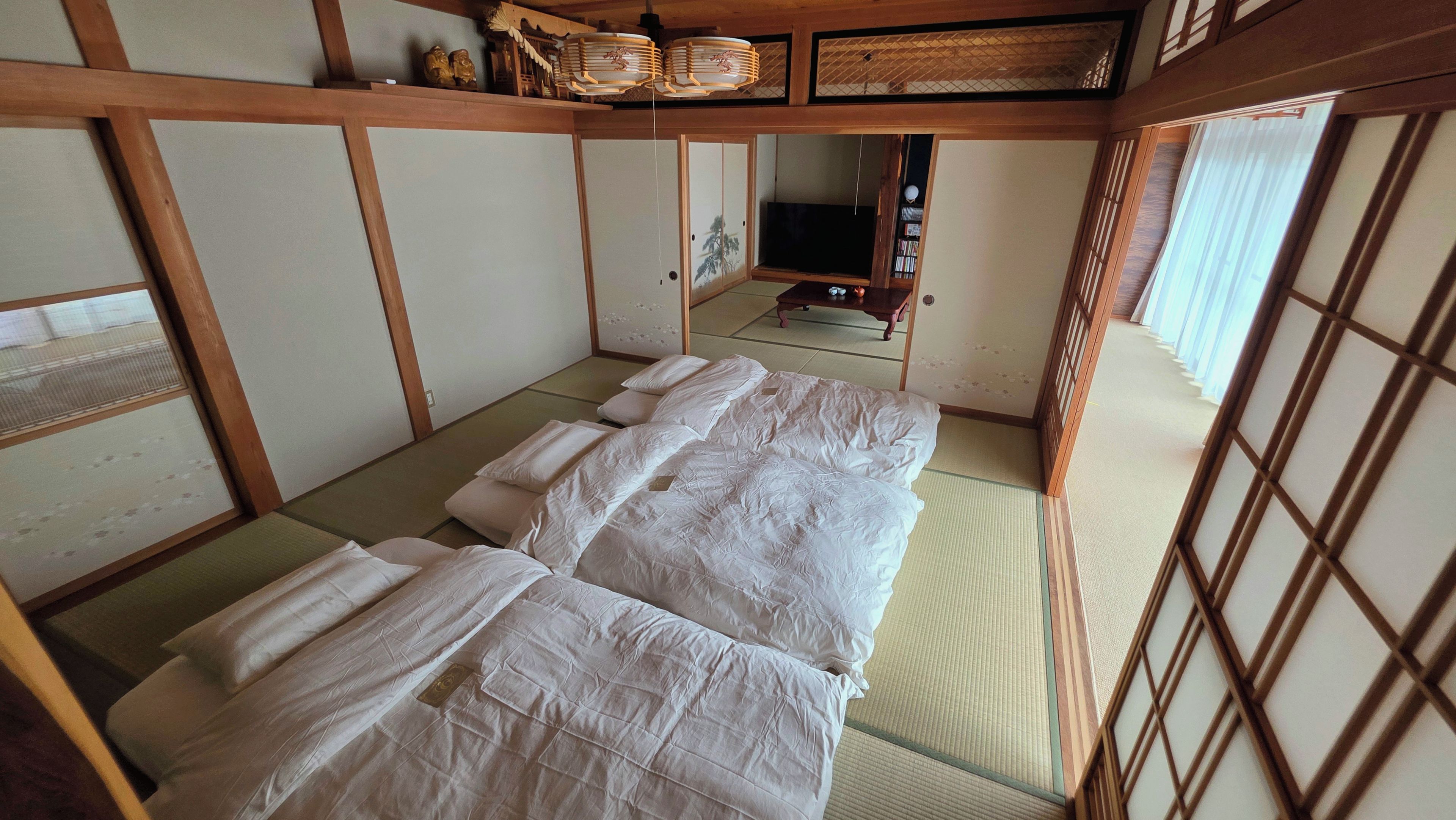 A traditional Japanese room with tatami flooring, a futon bed, sliding doors, and a television.