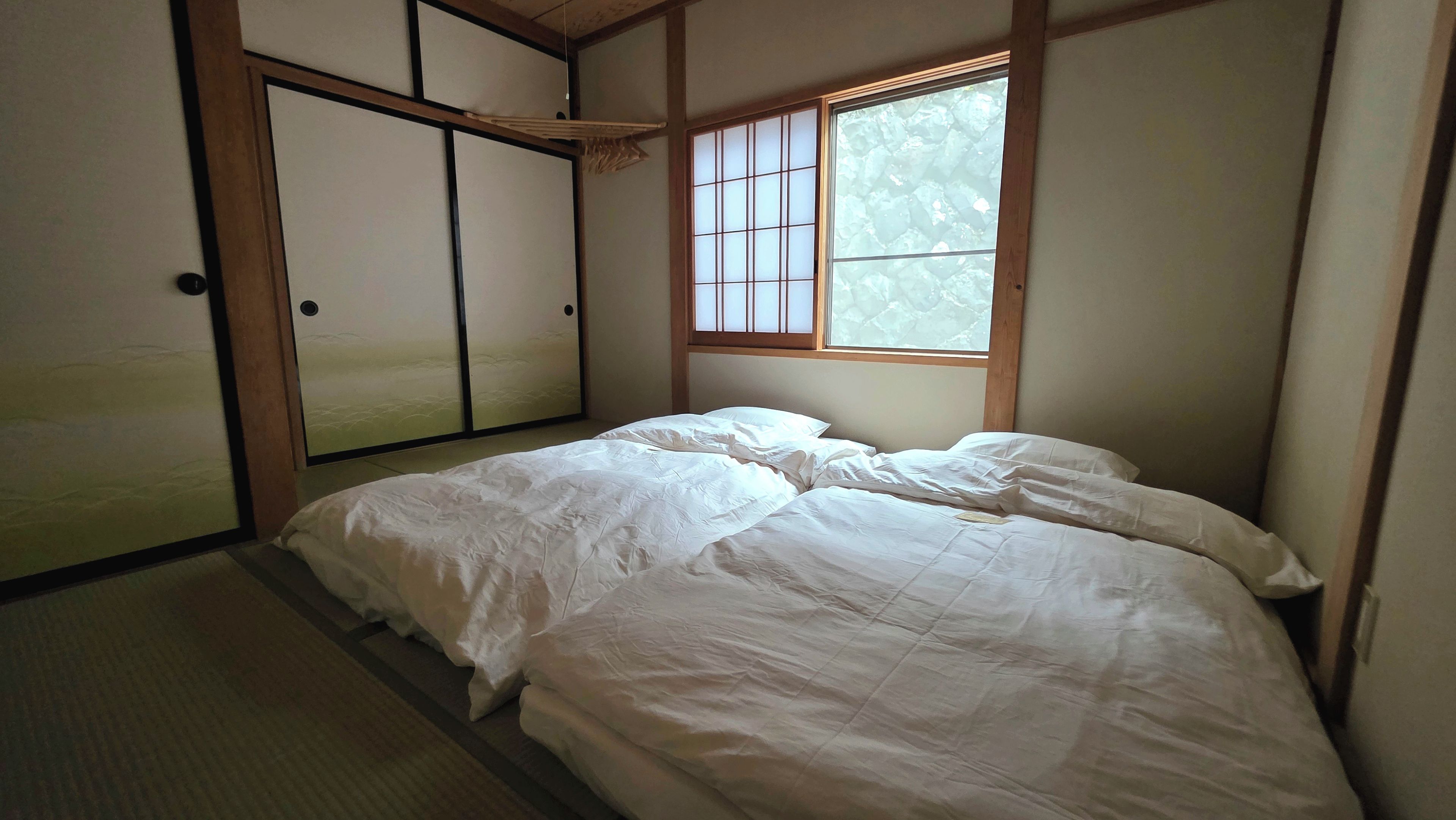 A traditional Japanese-style room with tatami flooring, a low bed with white bedding, and sliding shoji doors.