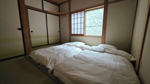 Perinteinen japanilaistyylinen huone, jossa on tatamimatto, matala sänky valkoisilla vuodevaatteilla ja liukuvat shoji-ovet.