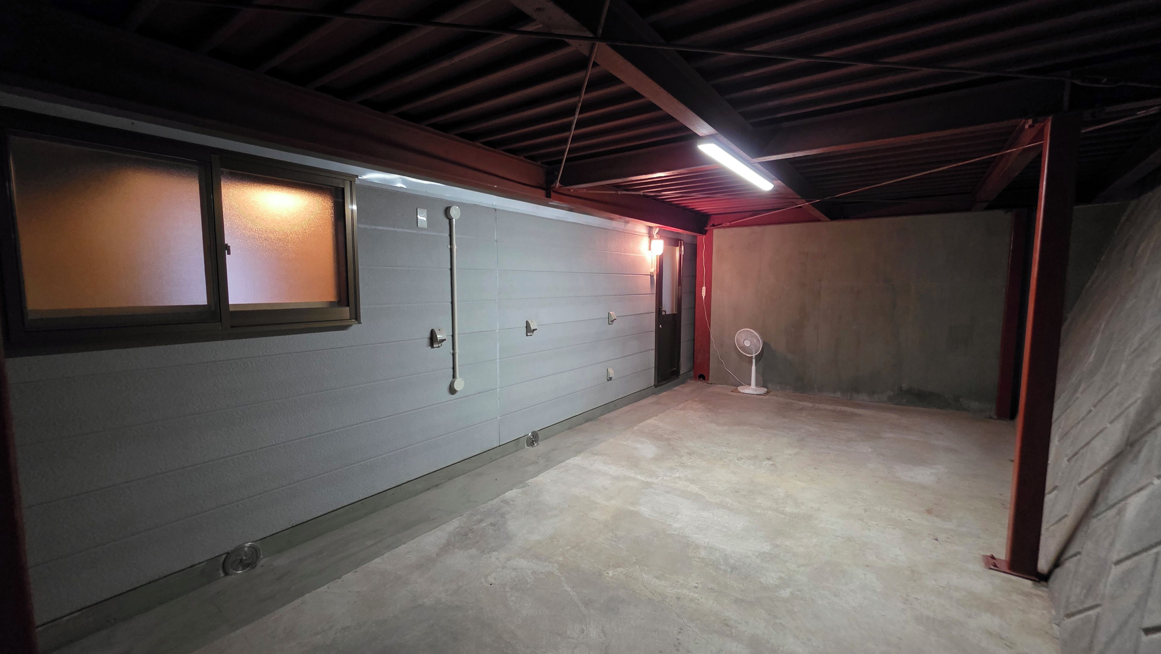 Un garage avec un sol en béton, une porte dotée d’une fenêtre et un ventilateur.