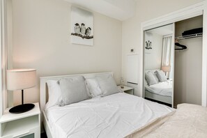 A neatly arranged bedroom with a bed, bedside lamp, and a mirror reflecting the room. - Modern 2BR 1.5BA + Free Parking, CN Tower, Jays! (Toronto)