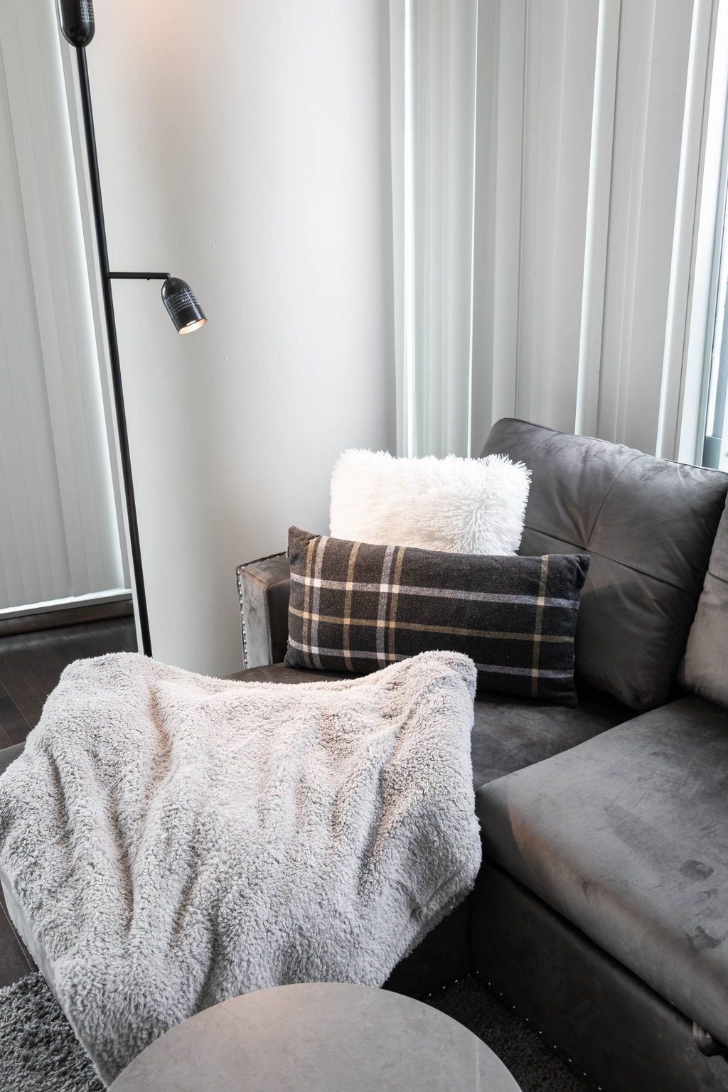 A modern living room with a grey sofa, a white fluffy throw, and a plaid pillow.