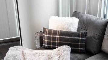 A modern living room with a grey sofa, a white fluffy throw, and a plaid pillow.