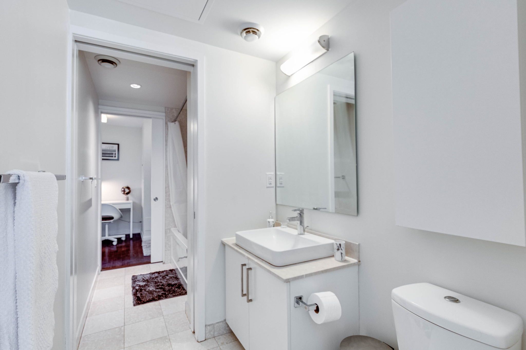 A modern bathroom with a white sink, mirror, and toilet.