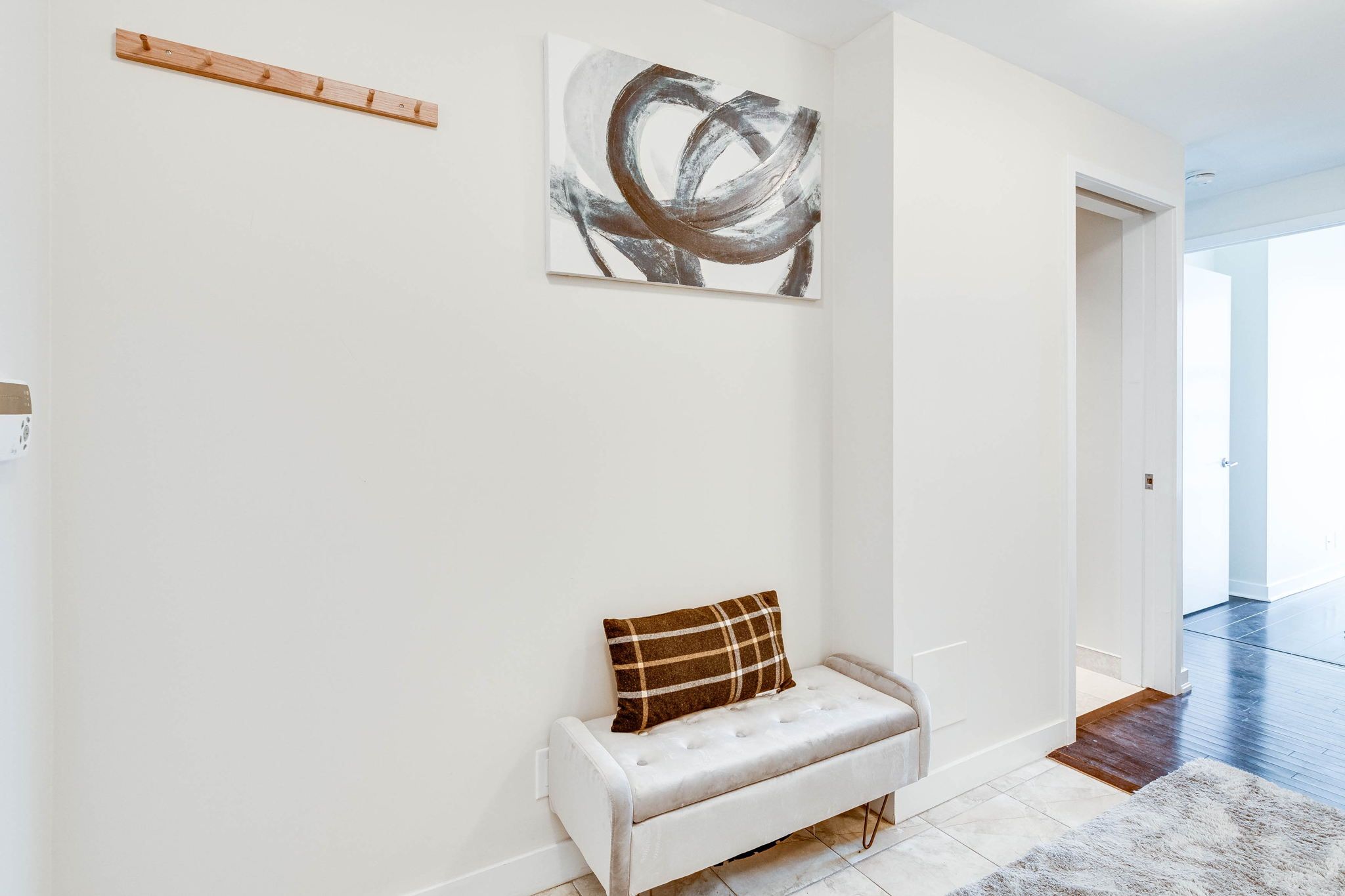 A modern interior with a white bench, a plaid pillow, and a large abstract painting on the wall.