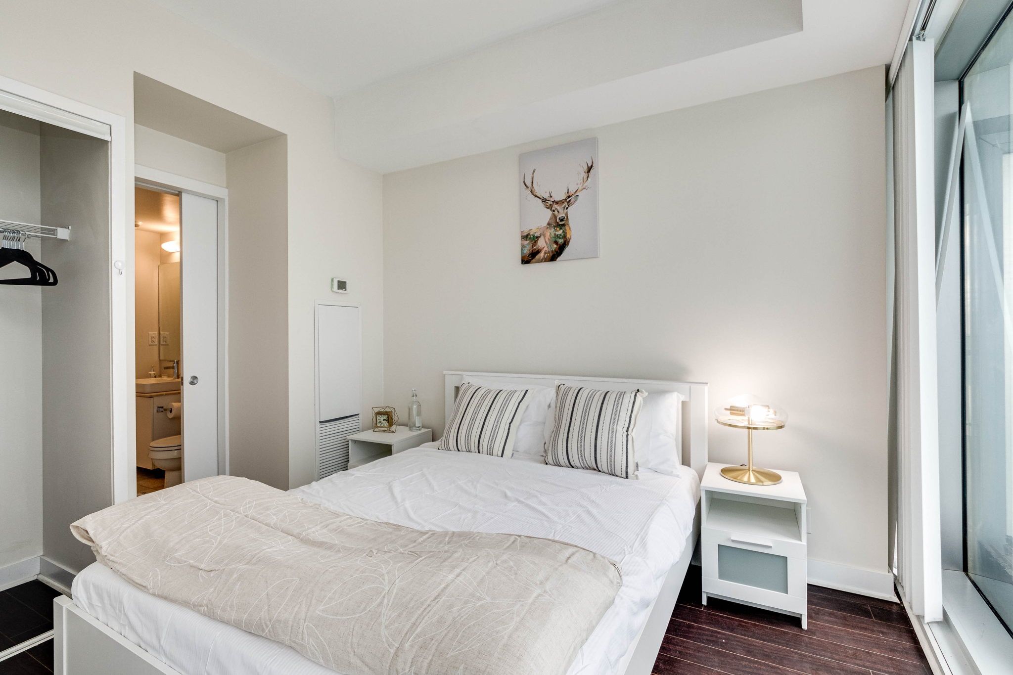 A bedroom with a bed, bedside tables, a clock, a deer's head decoration, and a window.
