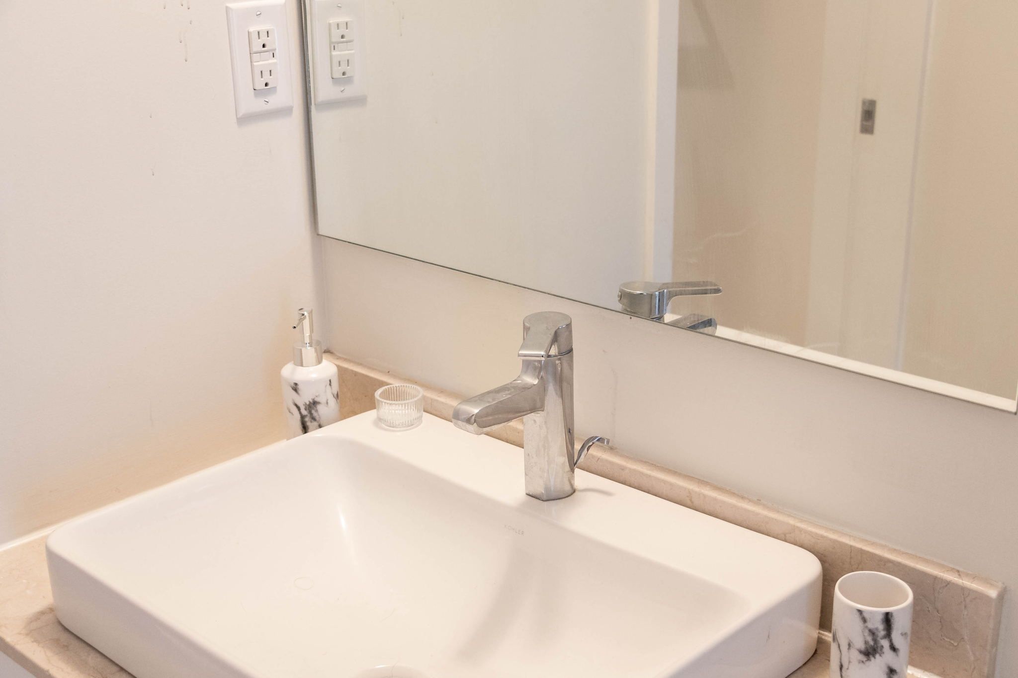 Een badkamer met een witte wastafel, een spiegel en een beker.