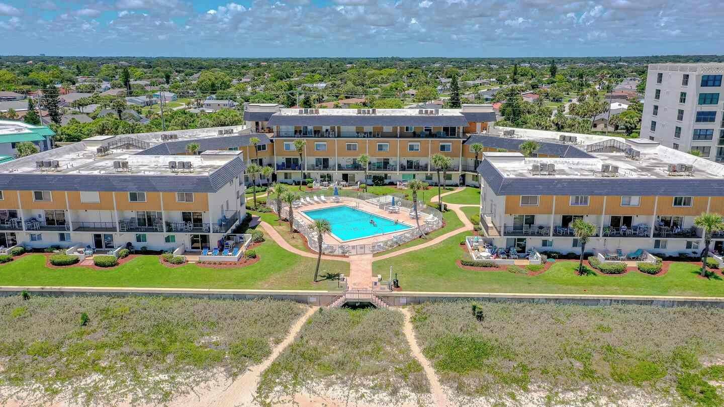 A multi-story hotel with a central swimming pool, surrounded by well-maintained lawns and a clear view of the surrounding area.
