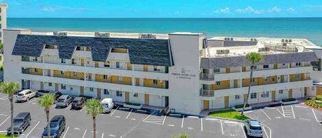 Een meerhoog hotel met een parkeerplaats ervoor, uitzicht op het strand en een bord waarop staat dat het een resort is.