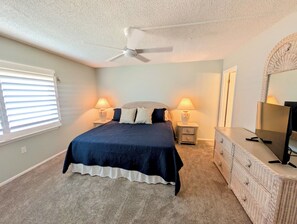 A bedroom with a bed, two bedside tables with lamps, a ceiling fan, a dresser, and a window with blinds. - Oceanfront Escape in Ormond Beach! (Ormond Beach)
