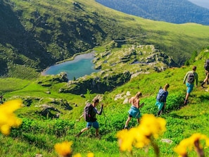 Eine Gruppe Wanderer auf einem grasbewachsenen Bergpfad, im Hintergrund ein See.