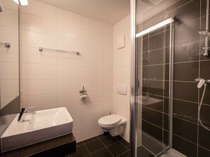 Ein Badezimmer mit weißem Waschbecken, WC und einer Duschkabine.