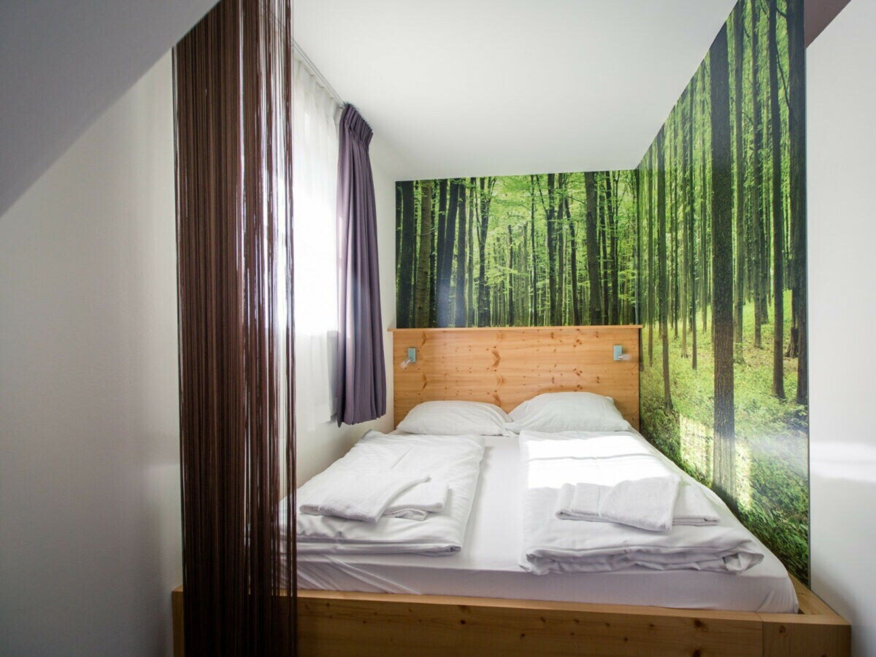 Een enkel bed met houten hoofdbord in een kamer met een wanddecoratie van een bos.