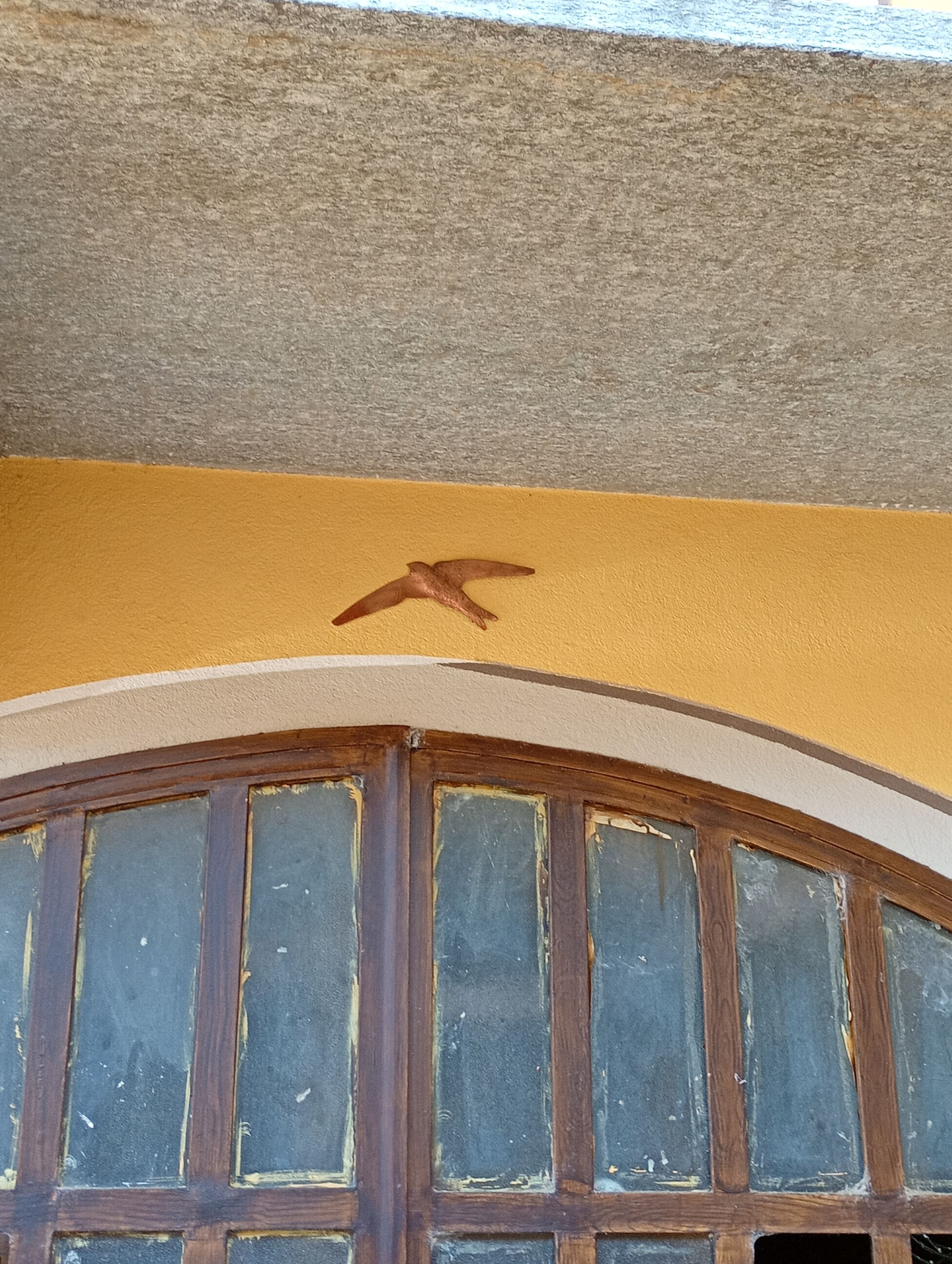Een kamer met een gele wand, een raam met houten kozijn en een vogelsticker.