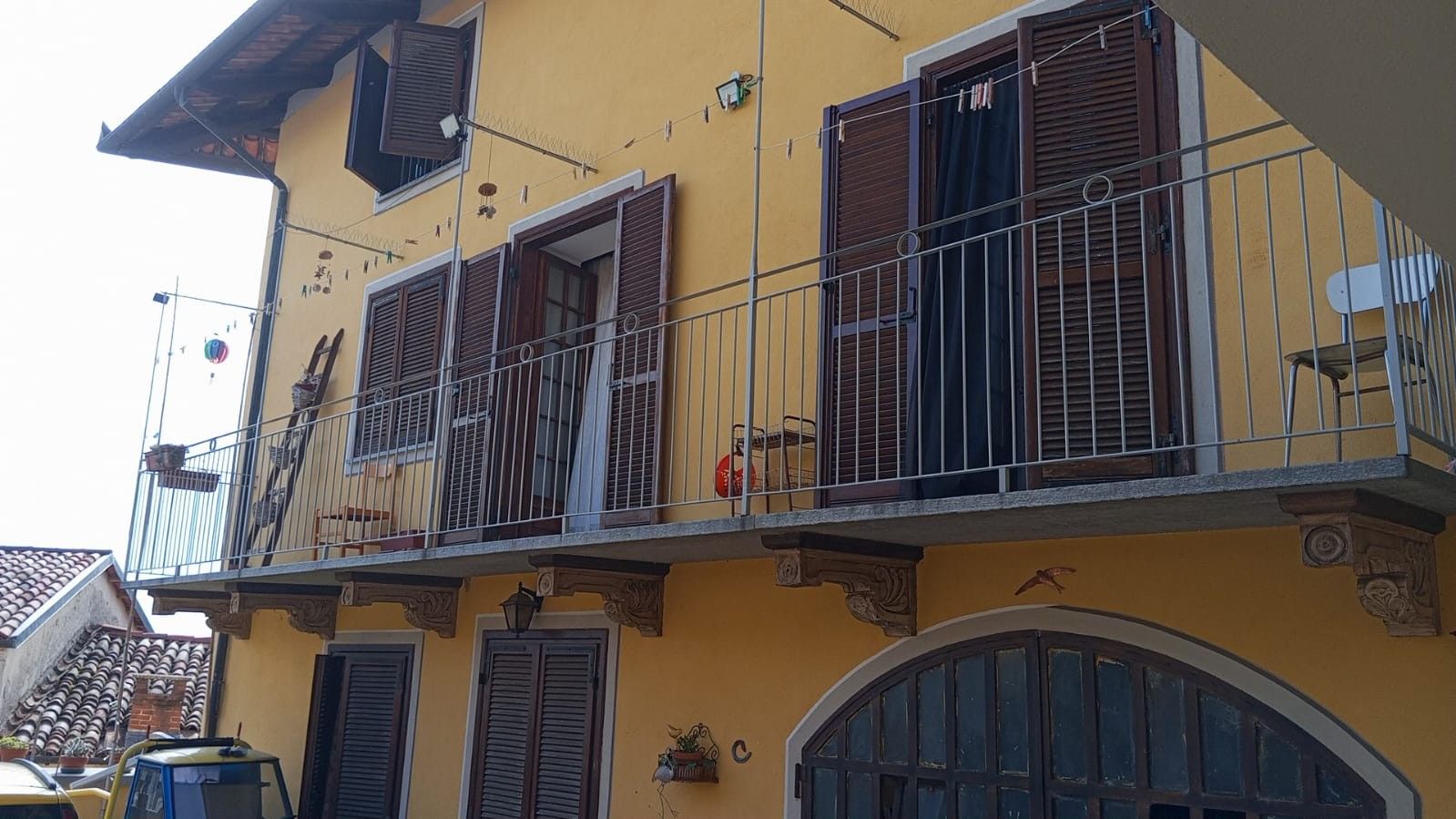 Un bâtiment jaune doté d’un balcon, de volets et d’un petit jardin.