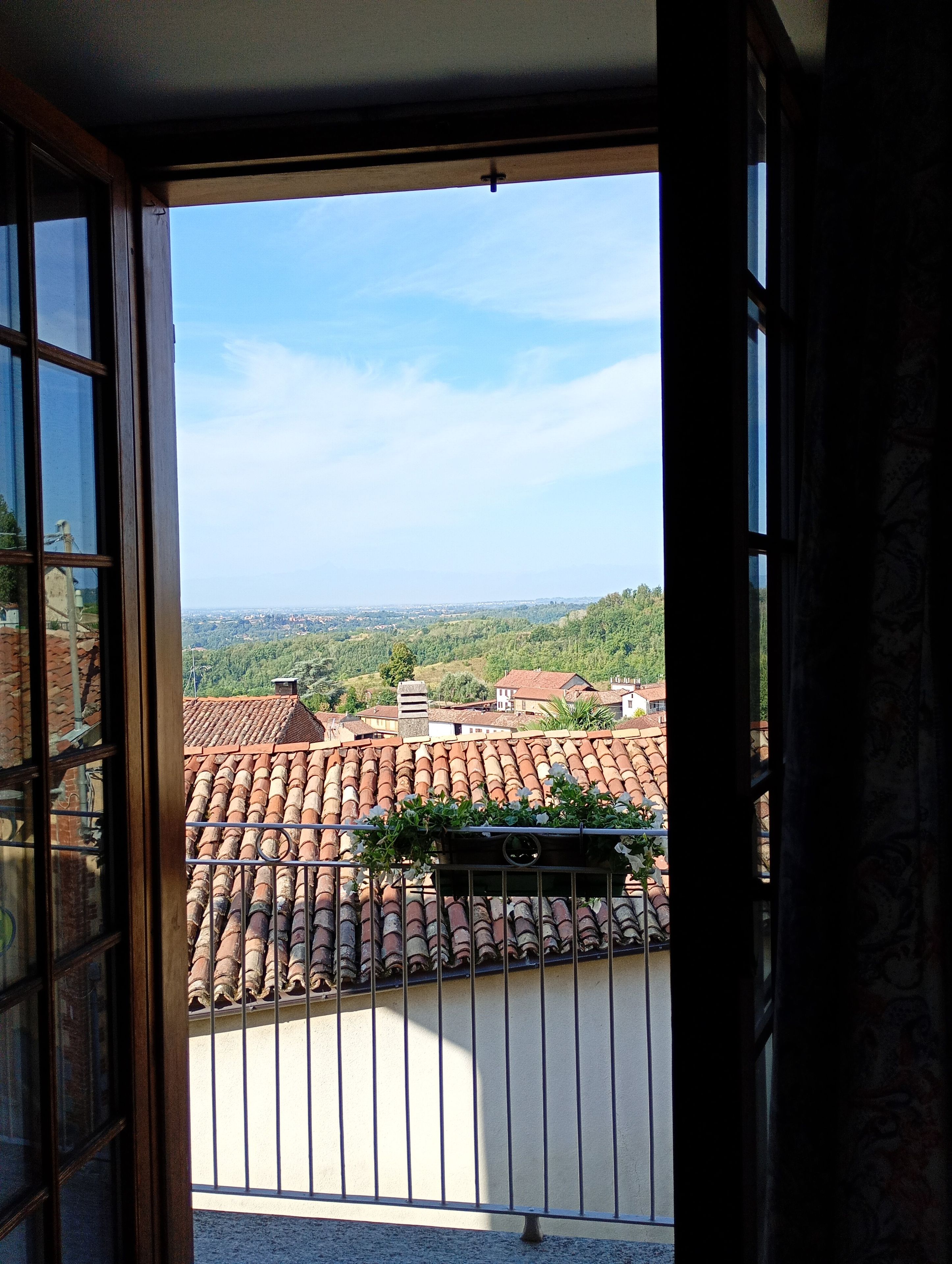 An open door revealing a balcony with a tiled roof and a view of a distant landscape.