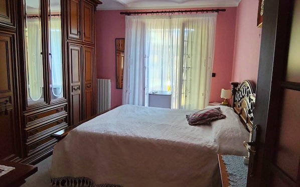 A bedroom with a large bed, a dresser, a mirror, and a window with curtains.