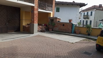 A paved courtyard with a brick floor, a yellow car, and a building with a balcony.