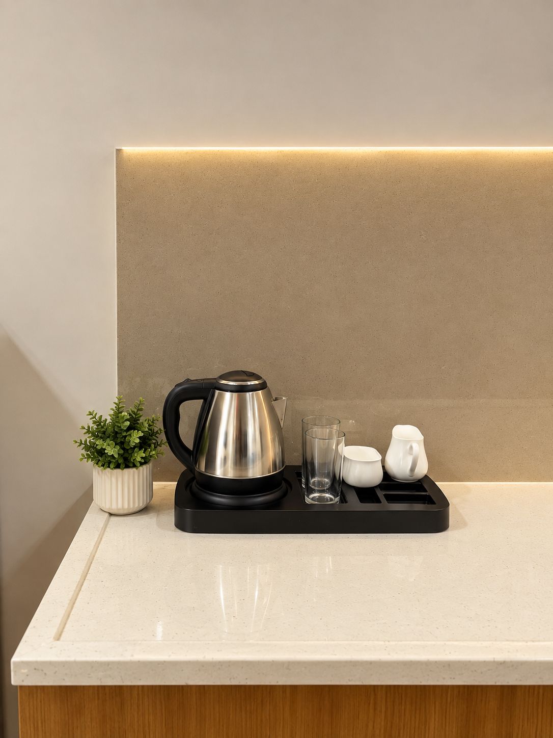A kitchen counter with a kettle, a potted plant, and a tray with cups and glasses.