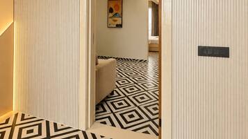 A hallway with a geometric patterned floor, a wooden ceiling, and a door leading to a room with a bed.