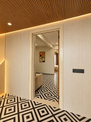 A hallway with a geometric patterned floor, a wooden ceiling, and a door leading to a room with a bed.