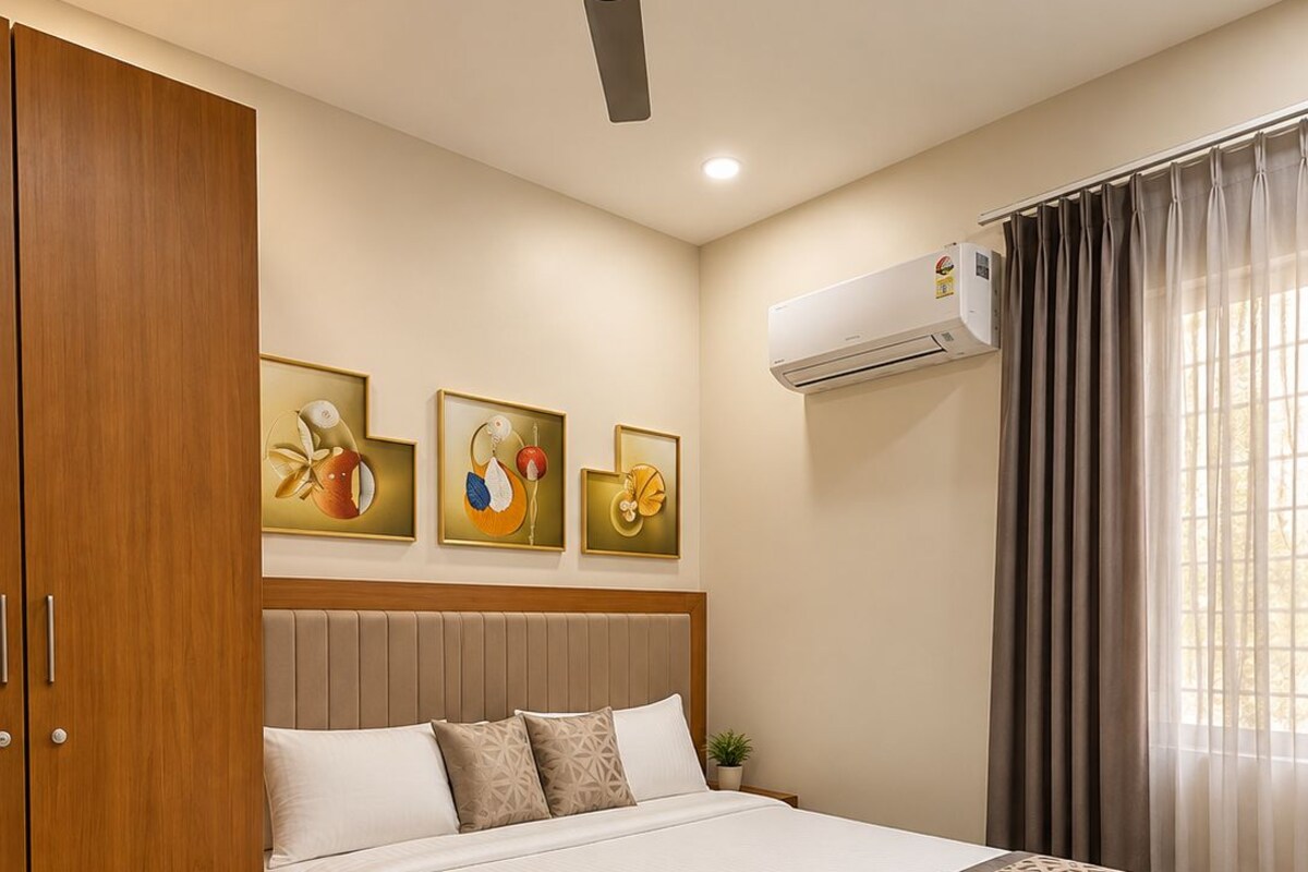 A hotel room with a bed, ceiling fan, air conditioning unit, artwork on the wall, and curtains.