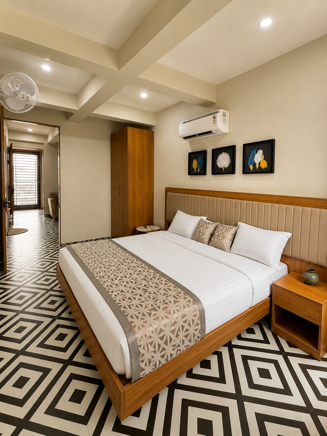 Una habitación de hotel moderna con una cama grande, una mesita de noche, un aire acondicionado instalado en la pared y una puerta que da a otra habitación.