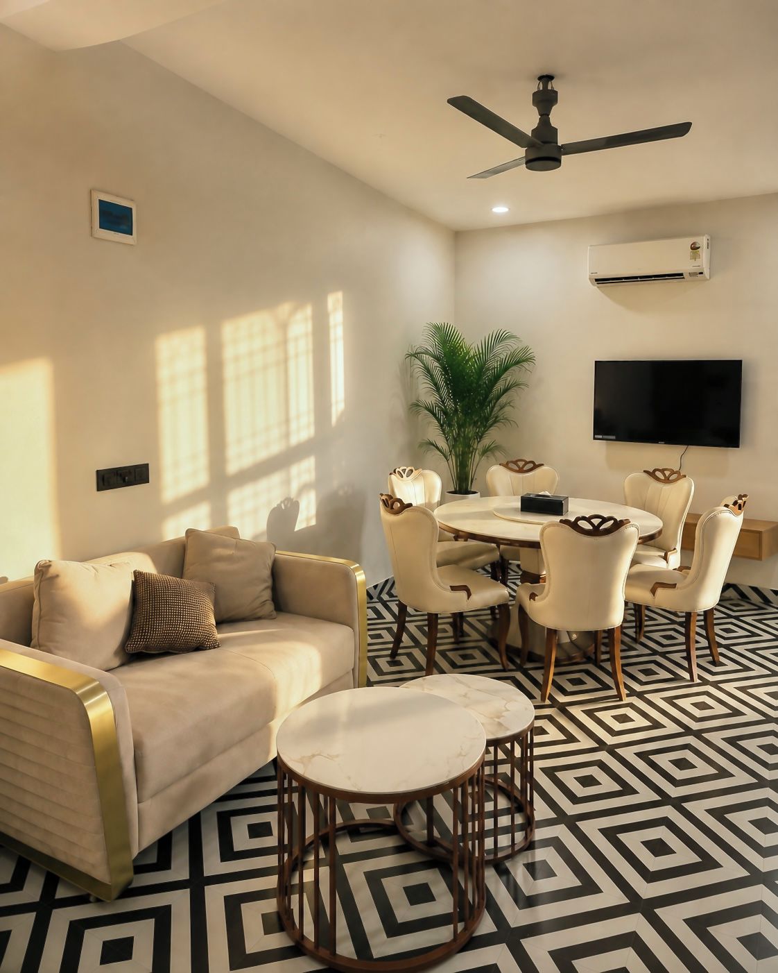 Una sala de estar con sofá, mesa de centro, mesa de comedor con sillas, ventilador de techo, televisor y planta en maceta.