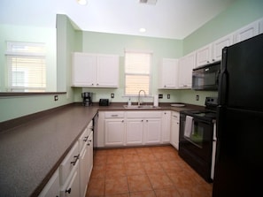 A kitchen with white cabinets, a black refrigerator, and a tiled floor. - Barb’s Stylish Digs: Modern Home+ Prime Location! (North Charleston)