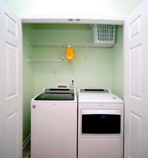 A laundry room with two white Whirlpool washers and dryers, a green wall, and a white door. - Barb’s Stylish Digs: Modern Home+ Prime Location! (North Charleston)