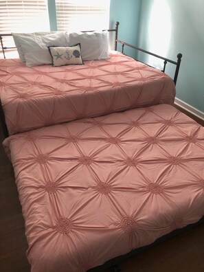 Ein Doppelbett mit einer rosa Tagesdecke und zwei Kissen, eines davon mit Muschelbild.