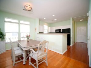 A dining area with a wooden table and chairs, a kitchen with white cabinets, and a white door. - Barb’s Stylish Digs: Modern Home+ Prime Location! (North Charleston)
