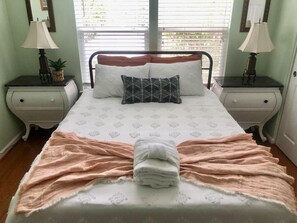 A neatly made bed with a folded towel in the center, flanked by two nightstands with lamps and a small plant on each. - Barb’s Stylish Digs: Modern Home+ Prime Location! (North Charleston)