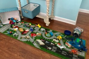 Ein detailliertes Miniaturmodell einer Stadtlandschaft mit Gebäuden, Fahrzeugen und einem kleinen Flughafen auf einem Teppich.