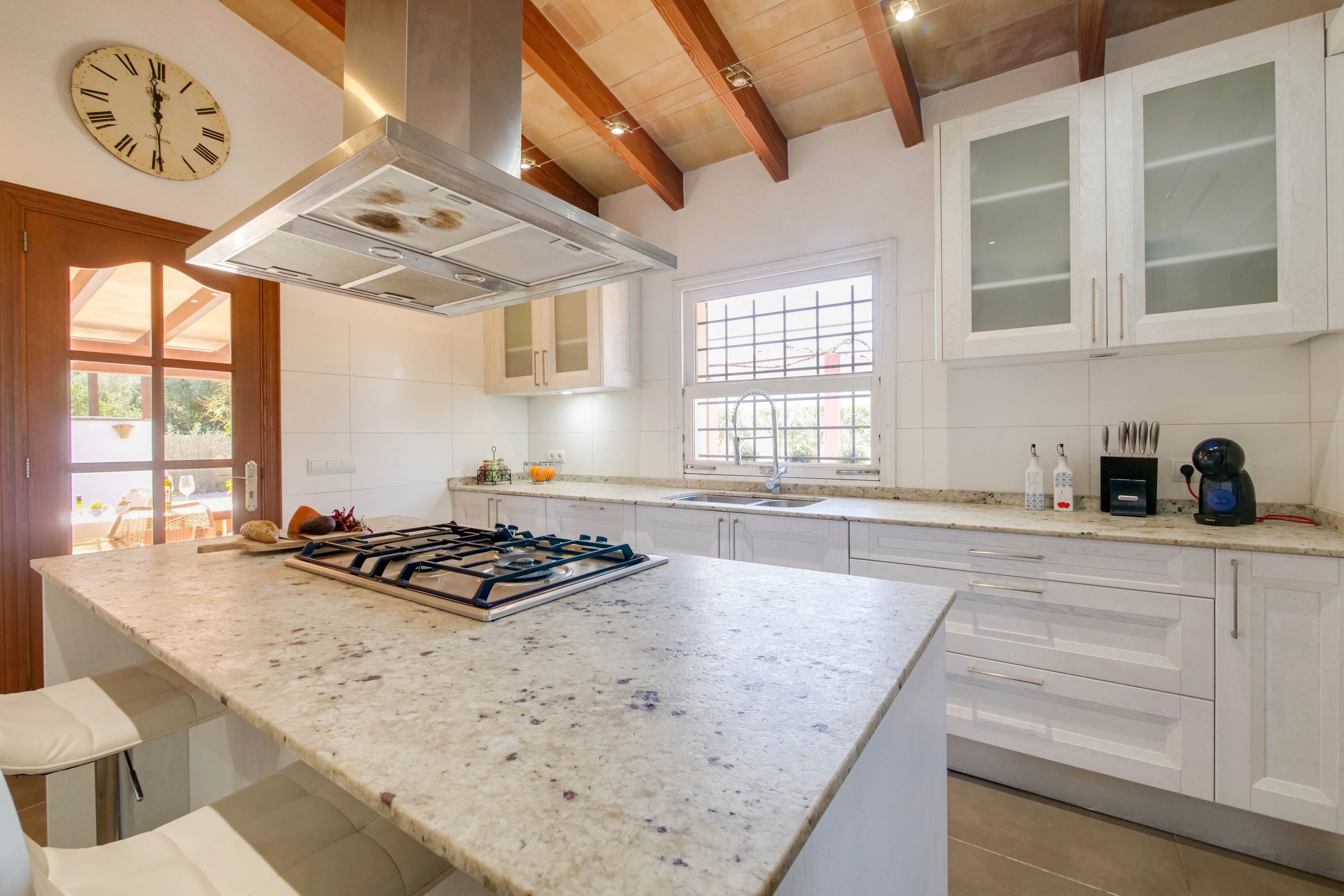 Una cocina moderna con una isla central, muebles blancos y una estufa empotrada.