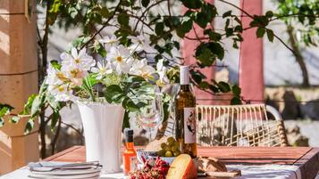 Una mesa servida con platos, una botella, una copa, una botella de vino, un bol de uvas, un trozo de queso y un jarrón con flores.