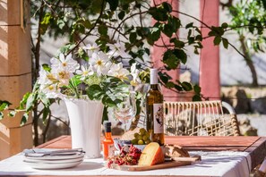 A table set with plates, a bottle, a glass, a bottle of wine, a bowl of grapes, a piece of cheese, and a vase with flowers. - Finca Reig – Vacation Home with Private Pool near Pollensa Beach (Illes Balears)