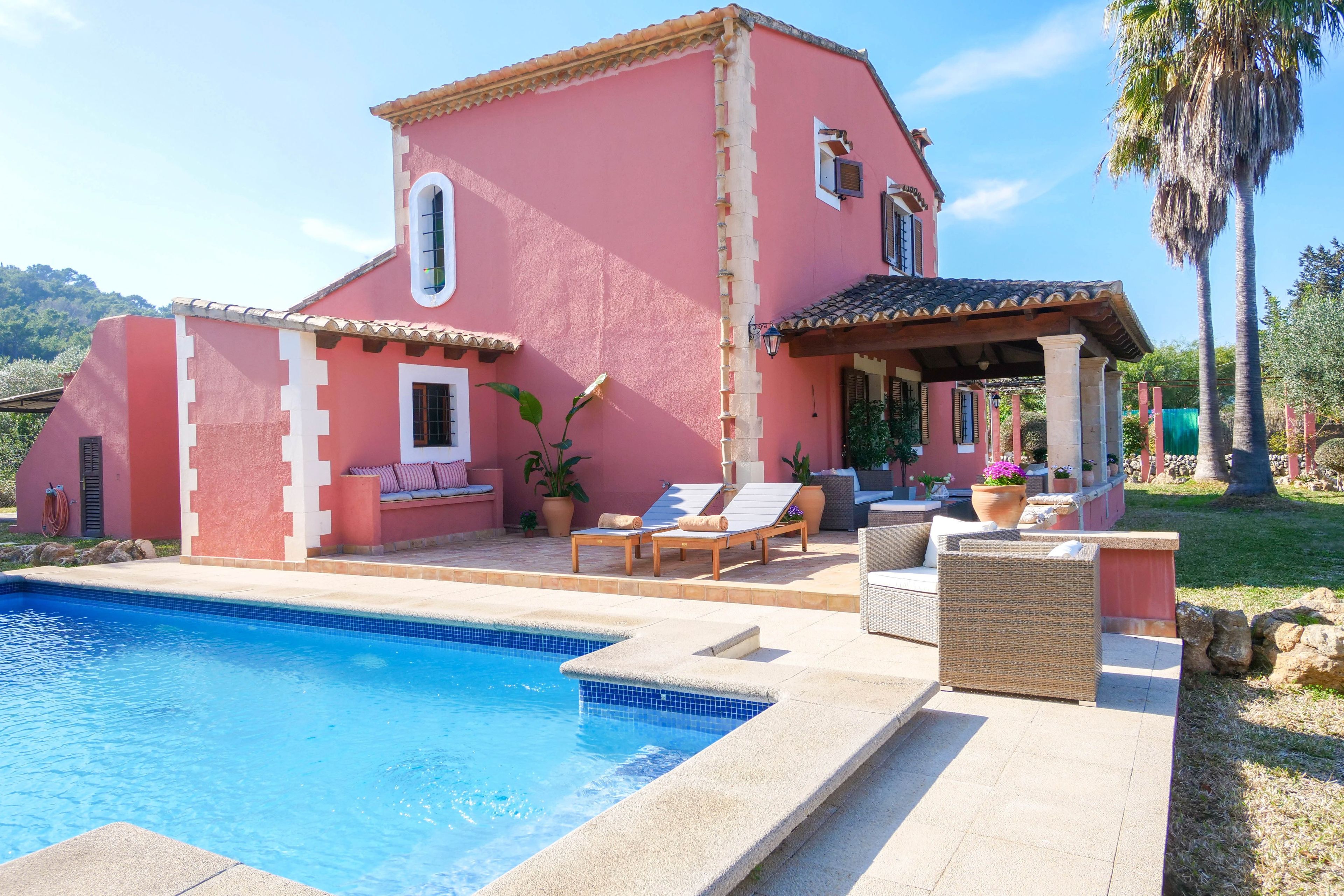 Una villa rosa con piscina, mobiliario exterior y jardín.