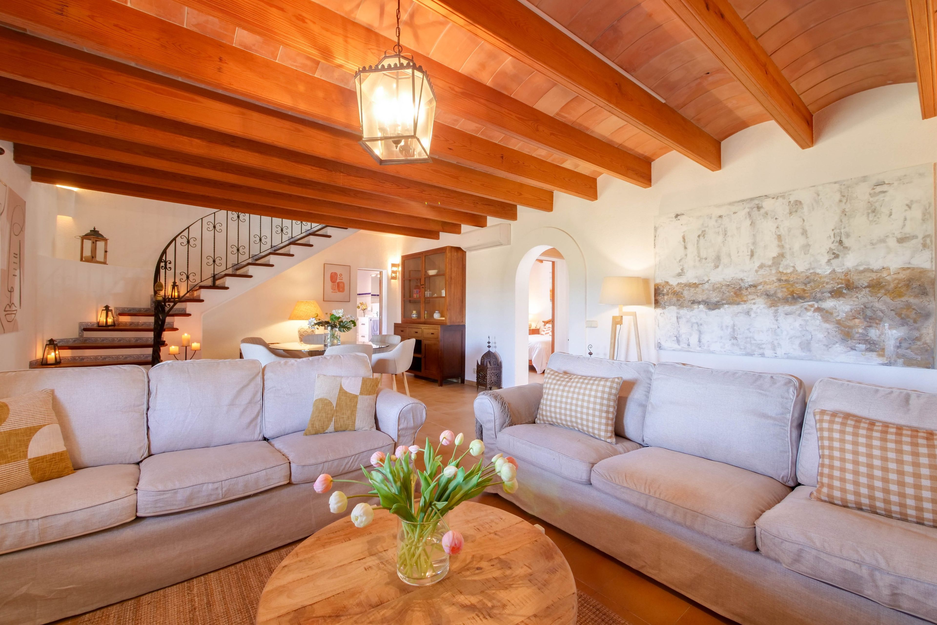 A spacious living area with a high wooden ceiling, a staircase, and a dining area.