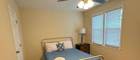 A bedroom with a bed, a ceiling fan, a window with blinds, and a door.