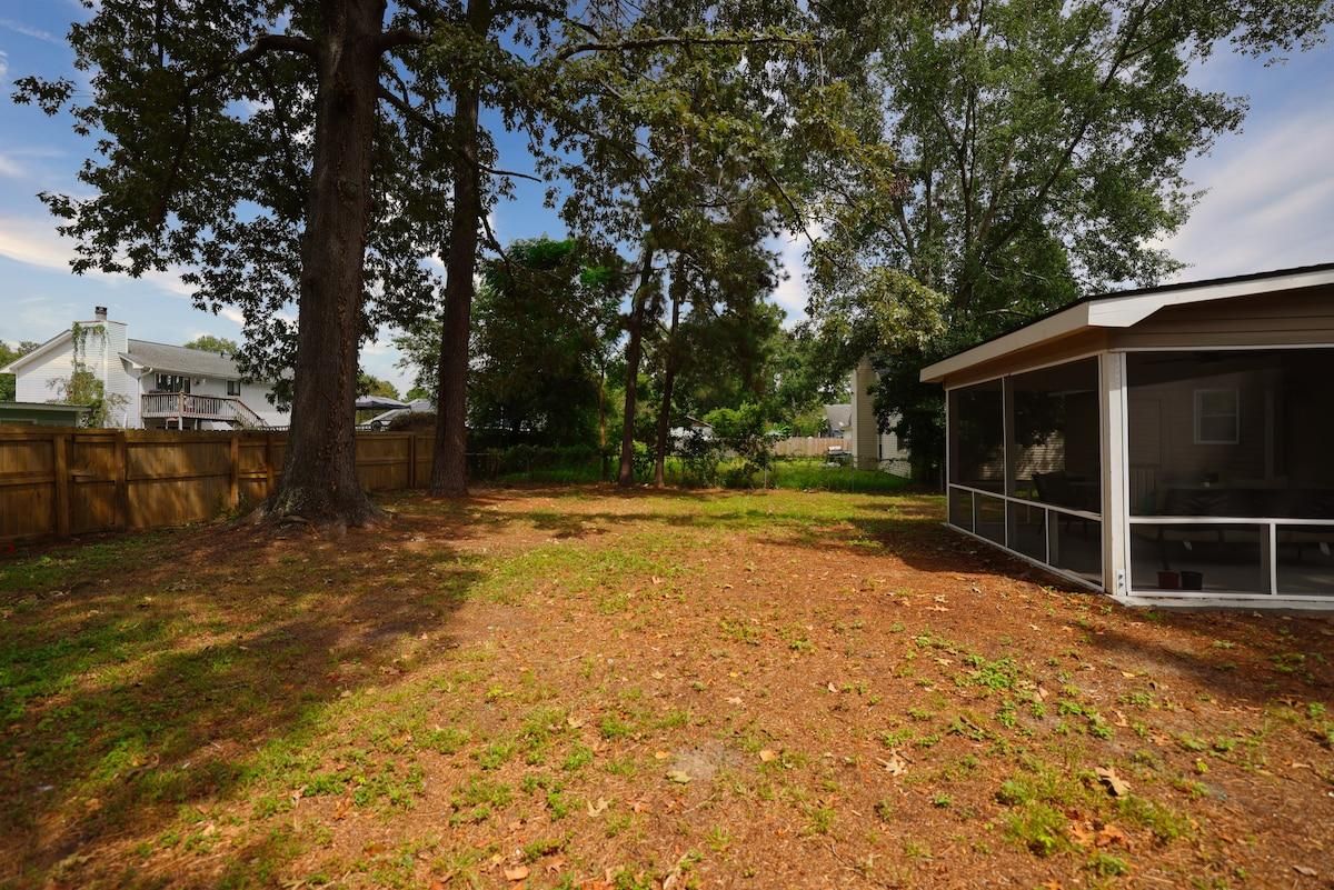 A backyard with a wooden fence, a large tree, and a covered patio area.