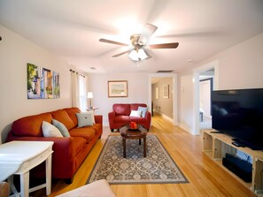 A living room with two sofas, a coffee table, a TV, and a ceiling fan. - Janelle’s Cottage: Walk to Brewery+Relax on Patio! (North Charleston)