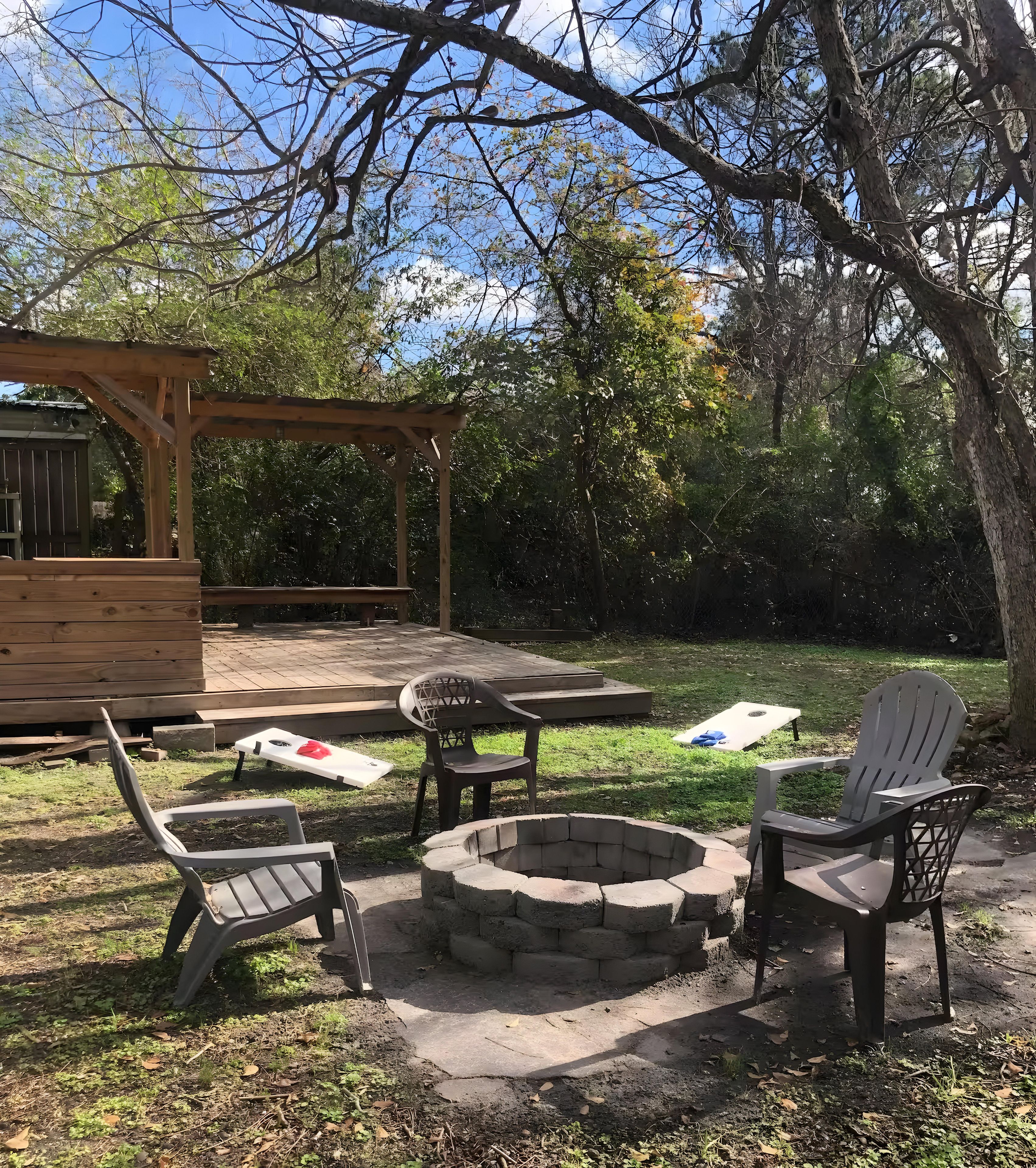 Een terras buiten, voorzien van een houten pergola, een vuurkorf en plastic stoelen.