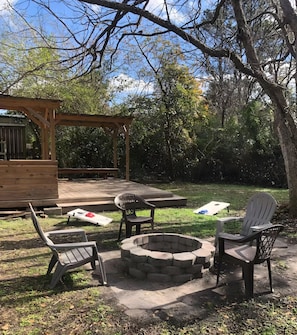 En uteplats med en träpergola, en eldstad och plaststolar.