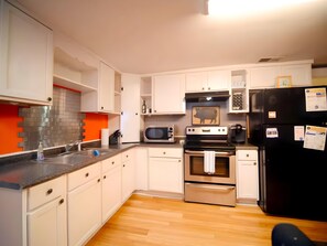 A kitchen with white cabinets, a stainless steel microwave, a black refrigerator, and a wooden floor. - Janelle’s Cottage: Walk to Brewery+Relax on Patio! (North Charleston)