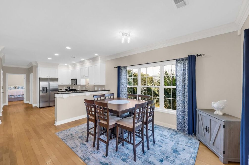 A modern kitchen with white cabinets, a central island, and a dining area with a round table and chairs.